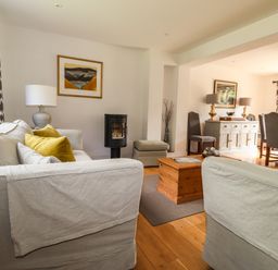 A living room with sofas coffee table and lamp opening into a dining area with chairs and sideboard at Ty Cerrig Newport Pembrokeshire