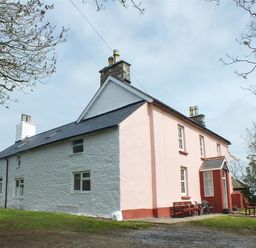 An exterior view of a large two-story house with white and pink walls a slate roof and outdoor seating on the front patio at Tremynydd Fawr in St Davids Pembrokeshire