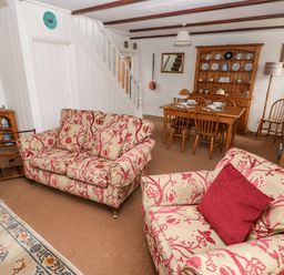 A living room with patterned sofas a dining table and chairs a wooden cabinet and staircase at Ty Canol in Mathry Pembrokeshire