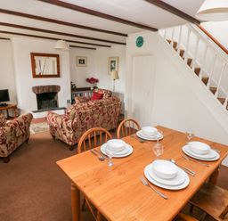 A dining table set for four and a sitting area with patterned sofas a fireplace and a television at Ty Canol in Mathry Pembrokeshire