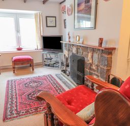 A sitting room with wooden armchairs with red cushions a stone fireplace a television and a window at Meadowlands in Dinas Cross Pembrokeshire