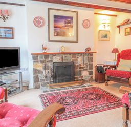 A living room with a stone fireplace red armchairs a television and framed pictures at Meadowlands in Dinas Cross Pembrokeshire