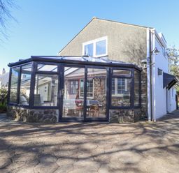 A conservatory with glass walls and a stone base attached to a two-story house at Meadowlands in Dinas Cross Pembrokeshire
