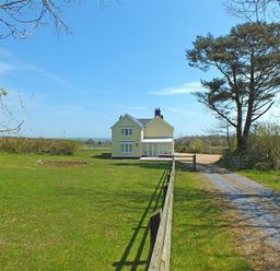 A yellow two-story house with a gravel driveway and fenced lawn under a blue sky at Sarnau in Efailwen Carmarthenshire