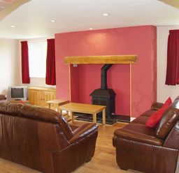 A living room with two brown leather sofas a wood burning stove and red curtains at Sarnau in Efailwen Carmarthenshire