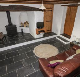 A living room with a leather sofa a rug a wood burning stove and a small television at Panteurig Cottage in Strumble Head Goodwick Pembrokeshire