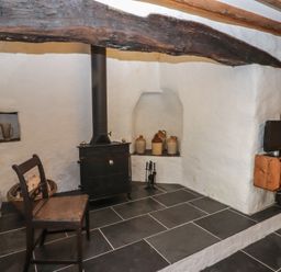 A corner with a wood stove black chair ceramic jugs and a small television on a wooden shelf at Panteurig Cottage in Strumble Head Goodwick Pembrokeshire