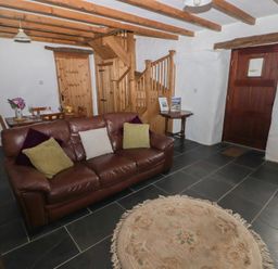 A living room with a leather sofa and pillows a round rug visible wooden stairs and a dining table at Panteurig Cottage in Strumble Head Goodwick Pembrokeshire