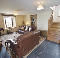 A living room with brown leather sofas a wooden staircase a bookshelf a television and a patterned rug at Panteurig Farmhouse in Strumble Head Goodwick Pembrokeshire