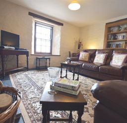 A living room with leather sofas a bookshelf a television on a wooden table and a patterned rug at Panteurig Farmhouse in Strumble Head Goodwick Pembrokeshire