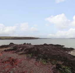 A rocky shoreline with water and distant land under a partly cloudy sky at Blackrock Boathouse in Dale Pembrokeshire