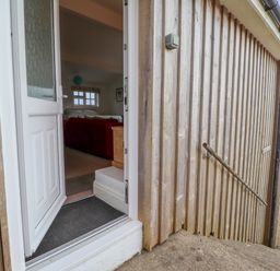 An open white door leading into a room with a red couch and a window overlooking the sea at Blackrock Boathouse in Dale Pembrokeshire