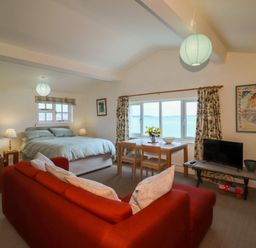 An open living space with a bed a red sofa a dining table with chairs and a television by a window at Blackrock Boathouse in Dale Pembrokeshire