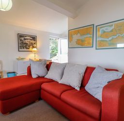 A red sectional sofa with four gray cushions in a room with framed maps and photographs on the walls at Blackrock Boathouse in Dale Pembrokeshire