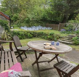 An outdoor seating area with wooden table and chairs on a patio surrounded by greenery at Yr Odyn in Llangrannog Ceredigion