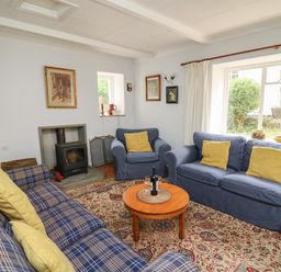 A living room with blue sofas yellow cushions a wood stove and a round wooden coffee table at Yr Odyn in Llangrannog Ceredigion
