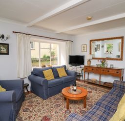A sitting room with blue sofas yellow cushions a wooden coffee table and a sideboard with a mirror at Yr Odyn in Llangrannog Ceredigion