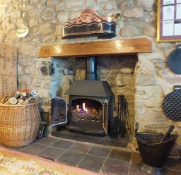 A stone fireplace with a wood burning stove and firewood basket at Granston Cottage in Castlemorris Pembrokeshire