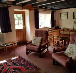 A living room with two armchairs a wooden dining table with chairs a side table with a lamp and two framed pictures on the wall at Granston Cottage in Castlemorris Pembrokeshire