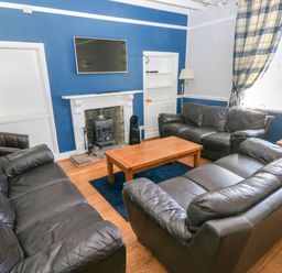 A living room with black leather sofas a wooden coffee table and a fireplace with a mounted TV at Newton West Farm in Newton near Newgale