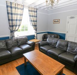 A living room with two black leather sofas a wooden coffee table checked curtains and a brown armchair at Newton West Farm Newton near Newgale
