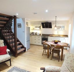 A kitchen and dining area with wooden table and chairs and stairs in a living space at Beach Cottage in Little Haven Pembrokeshire