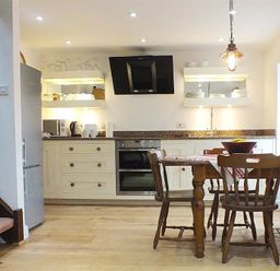 A kitchen with wooden chairs and table and appliances including oven refrigerator and kettle at Beach Cottage in Little Haven Pembrokeshire