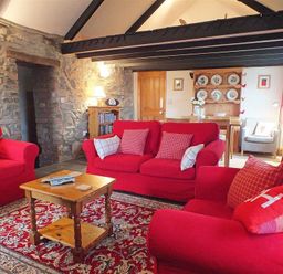 A living room with red sofas a wooden coffee table a stone wall and a wooden dresser with plates at Gwndwn Gwyn in Trefasser Near Strumble Head