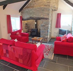 A living room with red sofas a stone fireplace wooden coffee table and a television at Gwndwn Gwyn in Trefasser Near Strumble Head