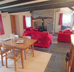 A dining and living area with a wooden table and chairs red sofas a stone fireplace and exposed wooden beams at Gwndwn Gwyn in Trefasser Near Strumble Head