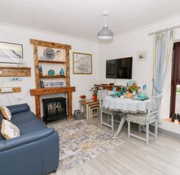 A living room with a blue sofa a dining table set for four a wall mounted TV and a window with striped curtains at 5 The Coach House Broad haven Pembrokeshire