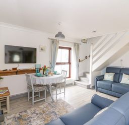 A living room with blue sofas dining table under window and stairs at 5 The Coach House in Broad haven Pembrokeshire
