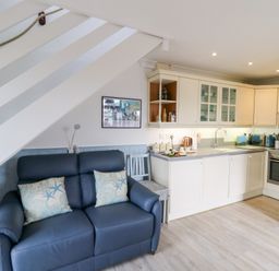 A kitchen with white cabinets and a blue sofa with cushions under a staircase at 5 The Coach House in Broad haven Pembrokeshire