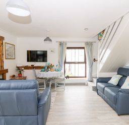 A living room with blue sofas a dining table under a window and a wall-mounted TV at 5 The Coach House in Broad haven Pembrokeshire