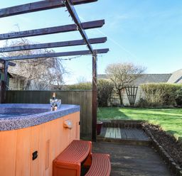 A garden with a hot tub and wooden pergola next to a grass lawn at Y Stabl in Fishguard Pembrokeshire