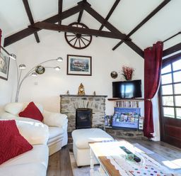 A living room with white sofas and red cushions a stone fireplace a television tourist information leaflets and red curtains at Y Stabl in Fishguard Pembrokeshire