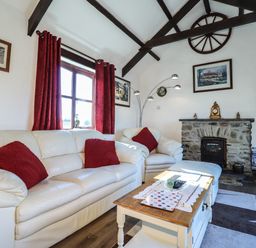 A living room with white sofas red cushions a stone fireplace and a wooden coffee table at Y Stabl in Fishguard Pembrokeshire
