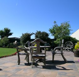 An outdoor patio with wooden chairs and table surrounded by plants and a lawn at Y Stabl in Fishguard Pembrokeshire