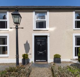 The front of a beige house with a black door two symmetrical windows and a black street lamp at The Rock House in Fishguard Pembrokeshire