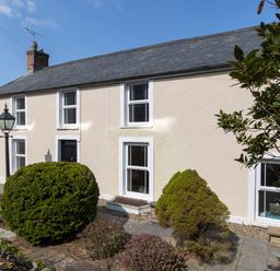The exterior of a two-story house with multiple windows a black front door shrubs and a stone pathway at The Rock House in Fishguard Pembrokeshire