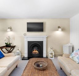 A living room with a fireplace two sofas a woven coffee table and a TV above the fireplace at The Rock House in Fishguard Pembrokeshire