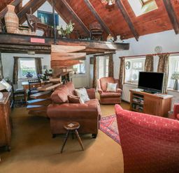 A living room with brown sofas a red armchair wooden furniture and spiral staircase at Ty-Newydd Cottage in Nevern near Newport Pembrokeshire