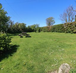 A grassy garden area with a wooden picnic table surrounded by bushes and trees at Ty-Newydd Cottage in Nevern near Newport Pembrokeshire