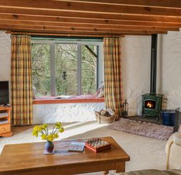 A living room with a wooden coffee table yellow flowers on it a window seat with cushions a fireplace and a television at Trawsnant Cottage in New Quay Ceredigion