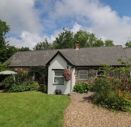 A cottage with a gravel pathway and garden with flowers at Trawsnant Cottage in New Quay Ceredigion
