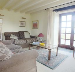 A living room with two sofas a glass coffee table a rug a television and French doors at Cockshead Cottage in St Dogmaels Pembrokeshire