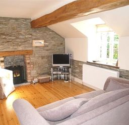 A living room with a grey sofa a armchair a television on a stand a stone fireplace and a window at Stable Cottage Cardigan in Cardigan Ceredigion