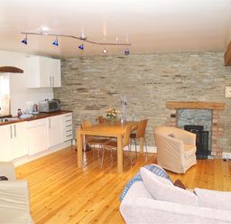 A kitchen and dining area with a wooden table and chairs stone wall and fireplace at Stable Cottage Cardigan in Cardigan Ceredigion