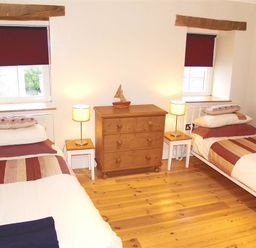 A bedroom with two single beds next to wooden dressers and two windows at Stable Cottage Cardigan