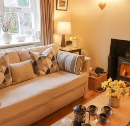 A living room with a sofa pillows a coffee table flowers a lamp and a fireplace at 1 Cheriton Row in Carew Cheriton Nr Tenby Pembrokeshire